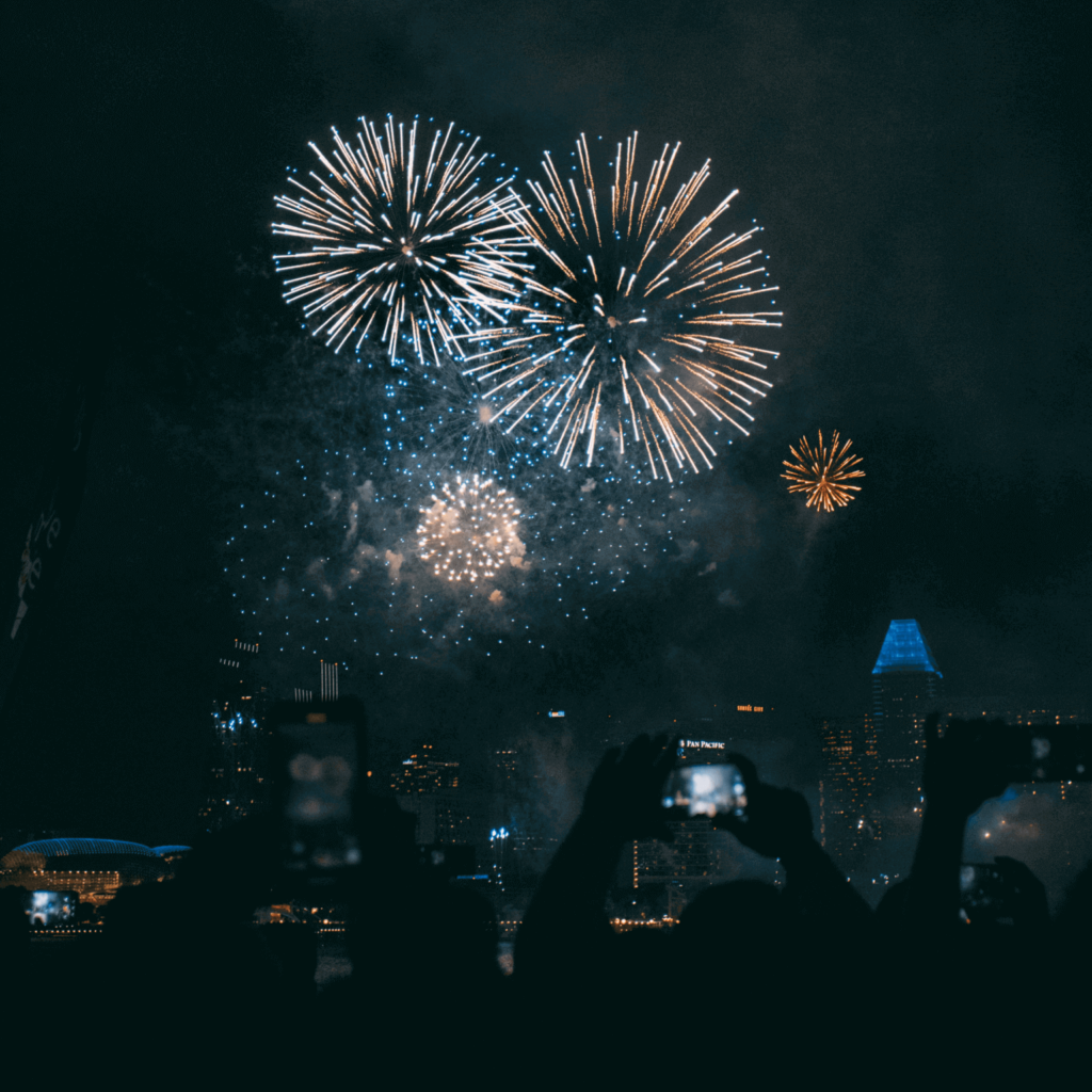 Picture of fireworks with people holding up their cameras in the foreground.