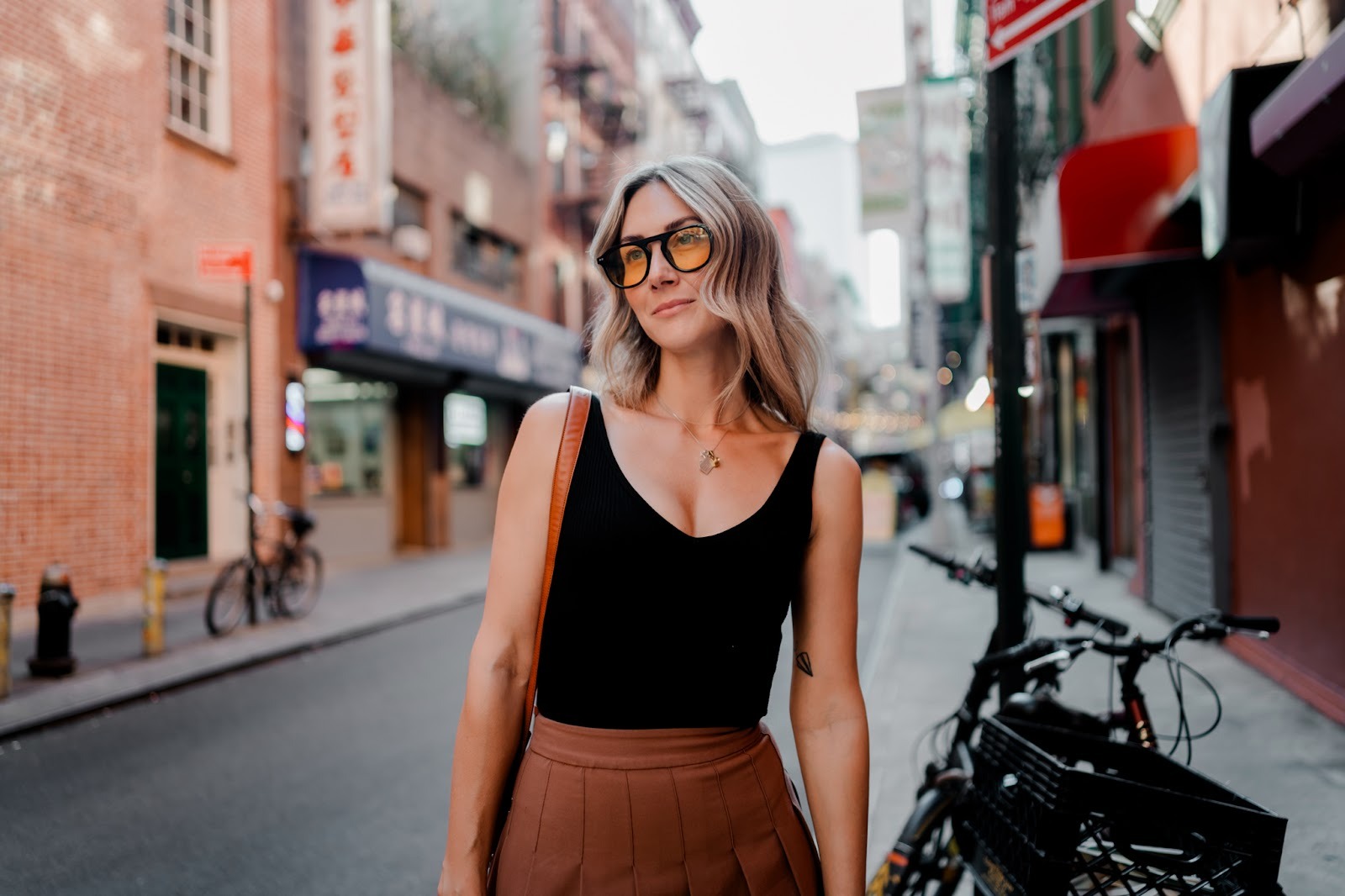 Woman standing on a city street near parked bicycles, photographed at close distance with storefronts and signs behind her. Shot with a 28mm lens by Esteban. 