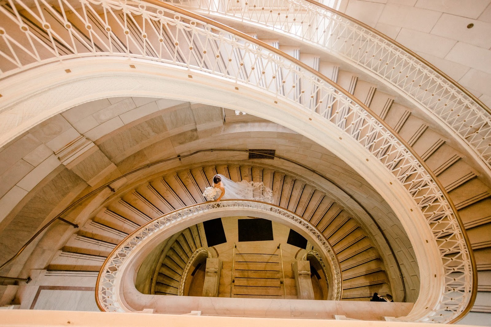 Spiral staircase interior photographed from above, with curved railings forming a circular pattern and a small figure on the landing. Shot with a 28mm lens by Esteban