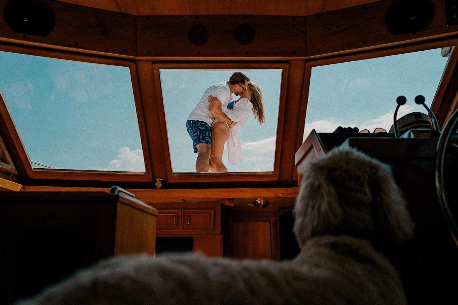 Couple kissing seen through a glass roof/skylight from inside a vehicle, with sky filling the frame. Shot with a 28mm lens by Esteban.