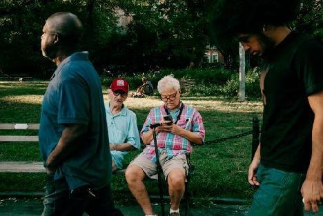 Park scene with people walking and sitting, photographed candidly with a shallow foreground and greenery behind. Shot with a 28mm lens by Esteban. 
